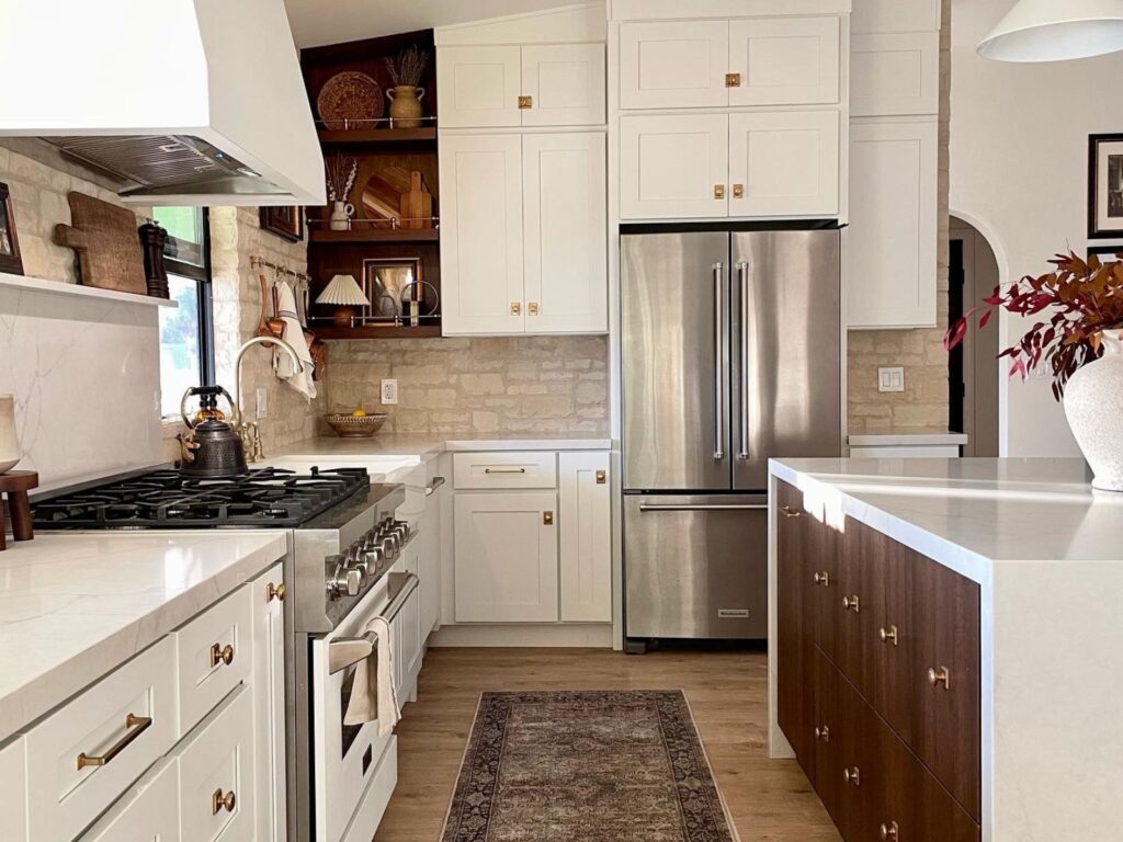 Renovated kitchen with white shaker cabinets, brass hardware, marble countertops, stone backsplash, and walnut island — a finished example of a thoughtfully budgeted home renovation.