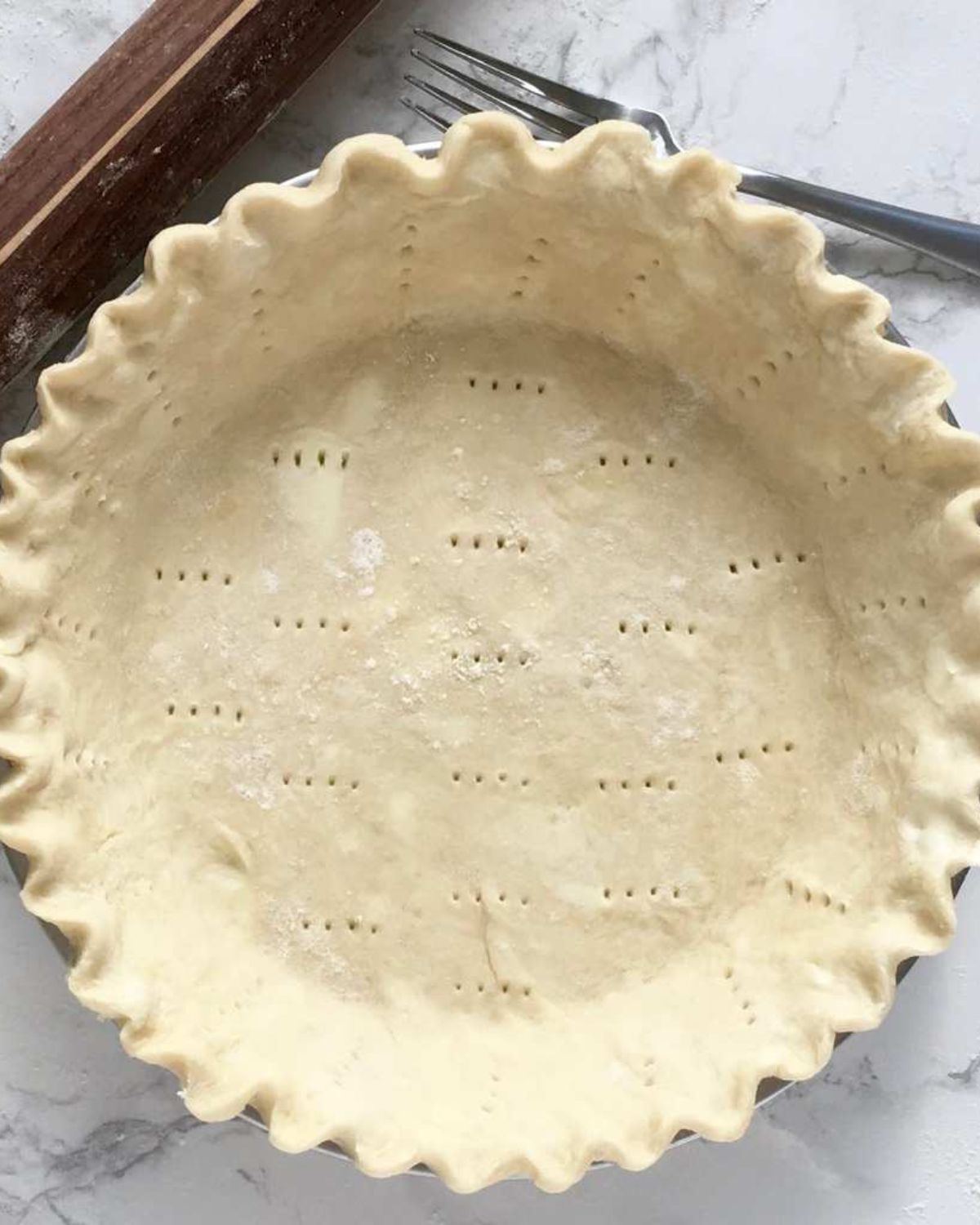 Unbaked homemade pie crust in a pie pan with a fluted crimped edge, docked with fork-pricked holes across the bottom to let steam escape during baking