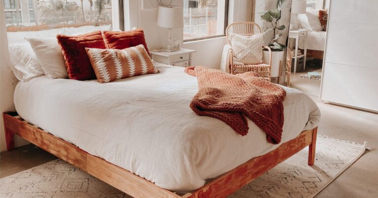 Refinished natural oak wood bed frame styled with white bedding, rust velvet pillows, a knit throw in a sunlit San Diego loft