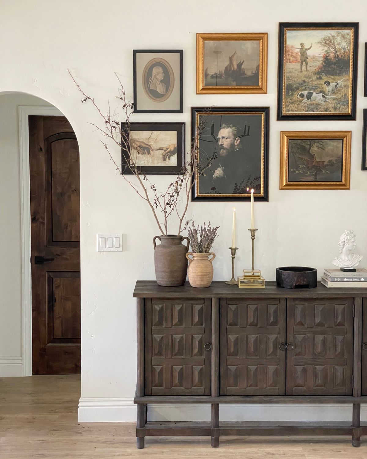 Dark carved wood console with gallery wall, terracotta vases, brass candlesticks, and classical bust — anchor piece interior design tip