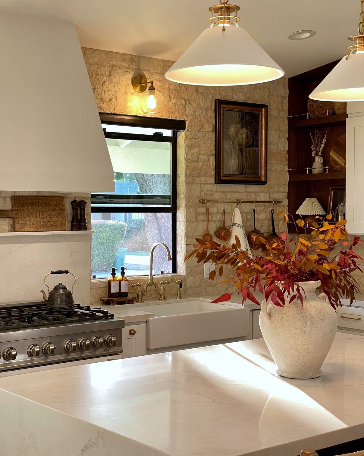Renovated kitchen with marble island, brass pendants, stone wall, and autumnal florals — interior design tips for beginners by Liz Lovery