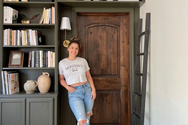 Liz Lovery in a Monterey graphic tee styled against a vintage bookshelf with brass accents and ceramic vases