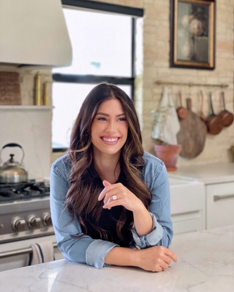 Liz Lovery in her warm, sunlit kitchen with copper pots and brick accent wall