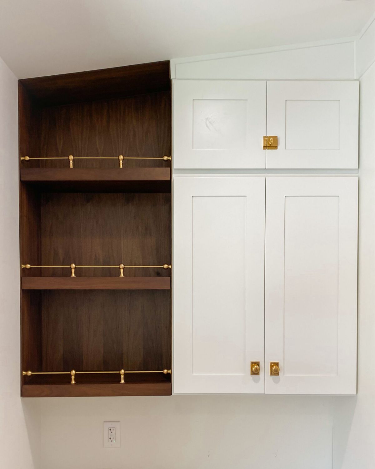 Walnut wood-panel kitchen shelves with brass gallery rails, next to white cabinets with brass hardware