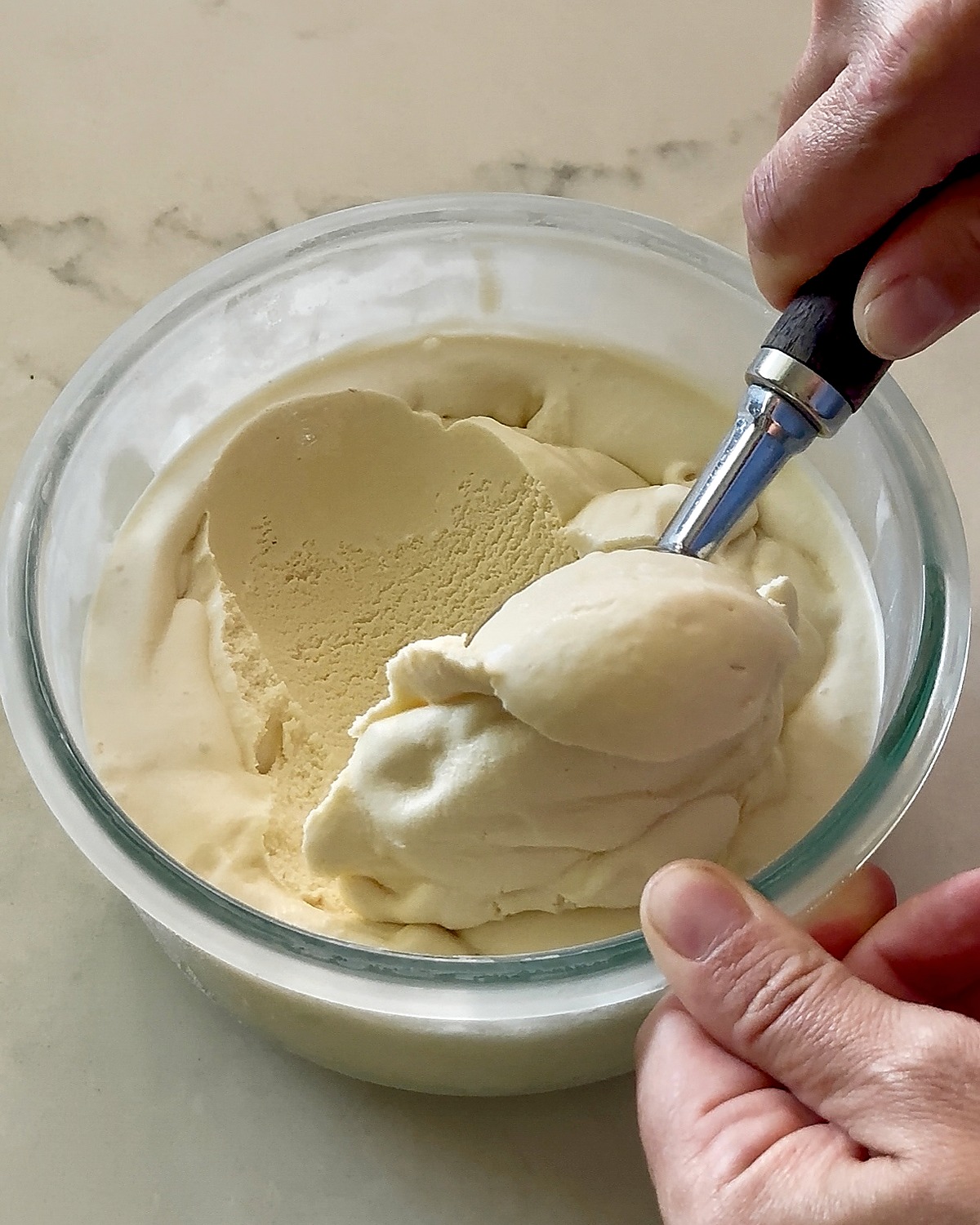 Scooping creamy homemade vanilla ice cream from a glass storage container