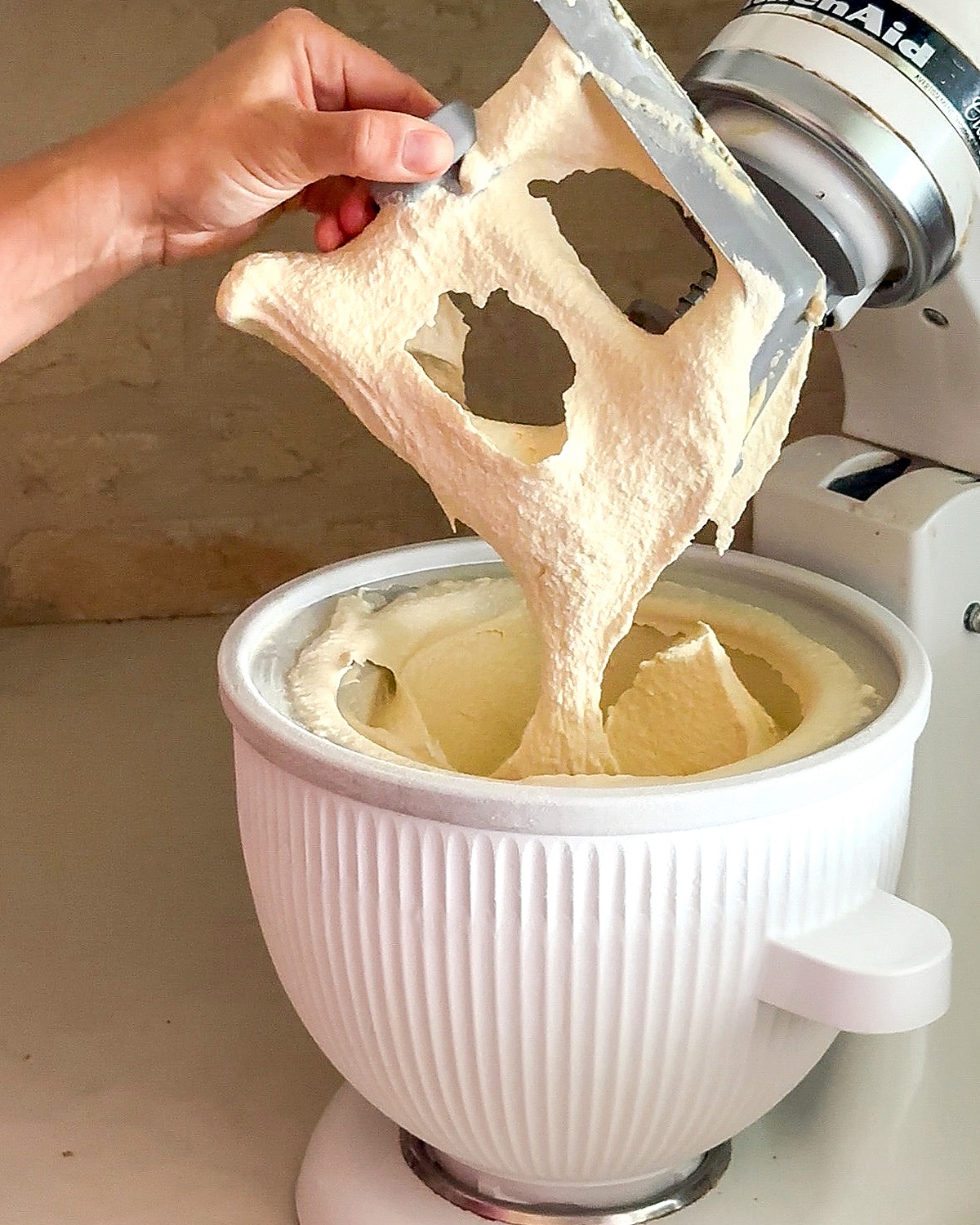 Thick homemade vanilla ice cream draping from the KitchenAid ice cream attachment paddle