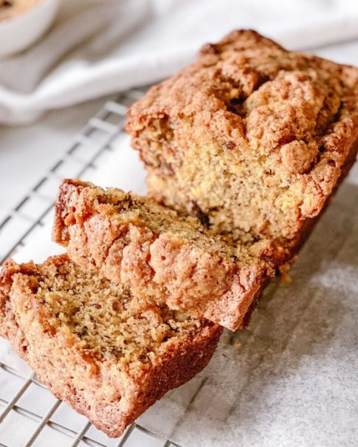 Close-up of a sliced super moist banana bread loaf on a wire rack, showing the cinnamon streusel crust and moist, tender crumb