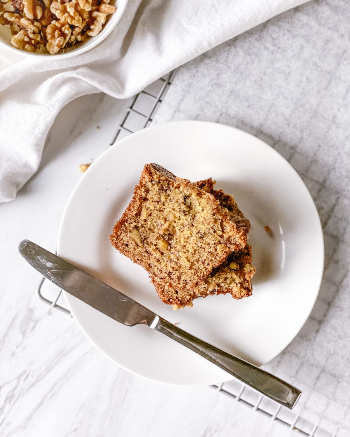 A single slice of super moist banana bread on a white plate, showing the tender crumb and walnuts, with a knife alongside