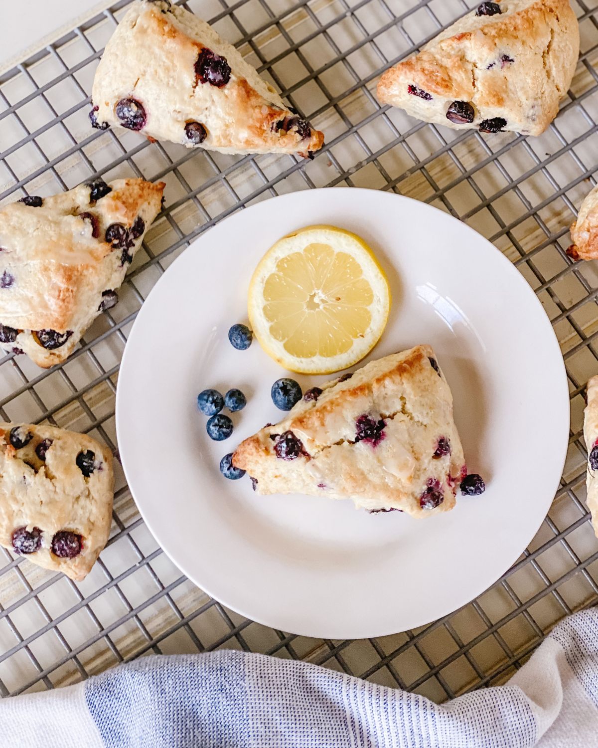 lemon blueberry scones on a white plate with a sliced lemon and fresh blueberries on a wire cooling rack