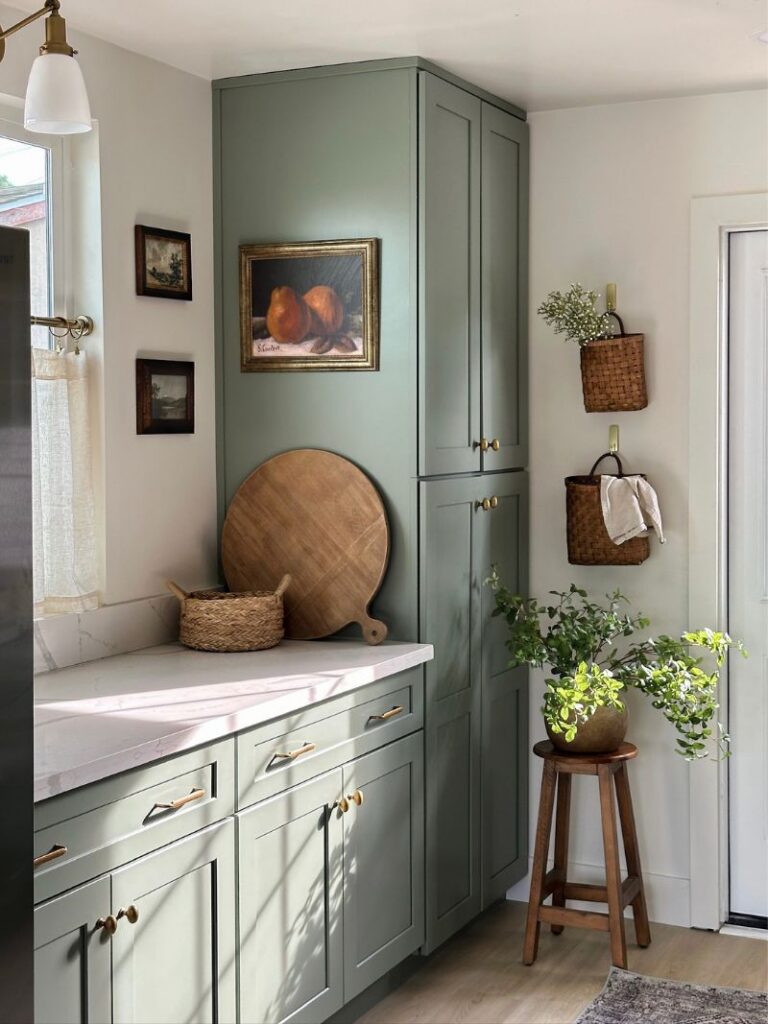 The Triplex renovation kitchen with sage green cabinetry, brass hardware, and vintage artwork