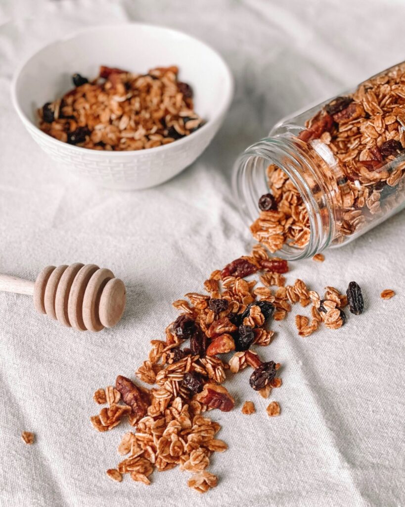 Pumpkin spice granola spilling from a jar next to a white bowl of granola on a linen cloth