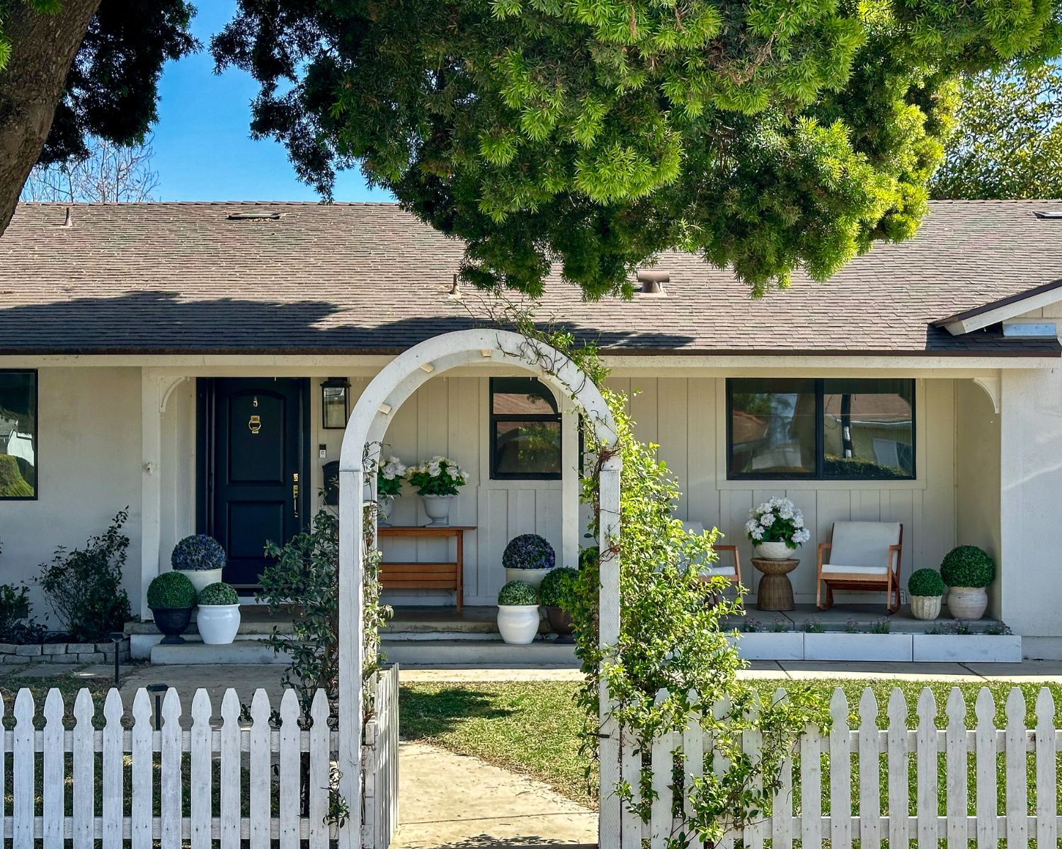 California ranch style home with front porch planters, white picket fence, and garden arbor