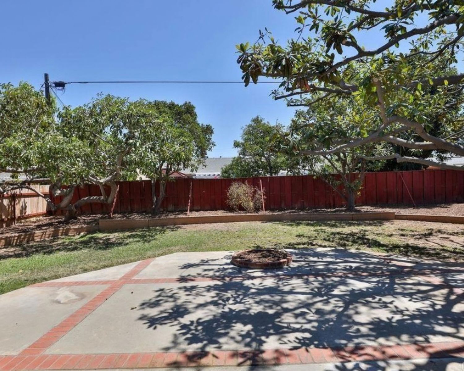 Original concrete patio with red brick borders, a round brick planter and a red wood fence before the backyard renovation