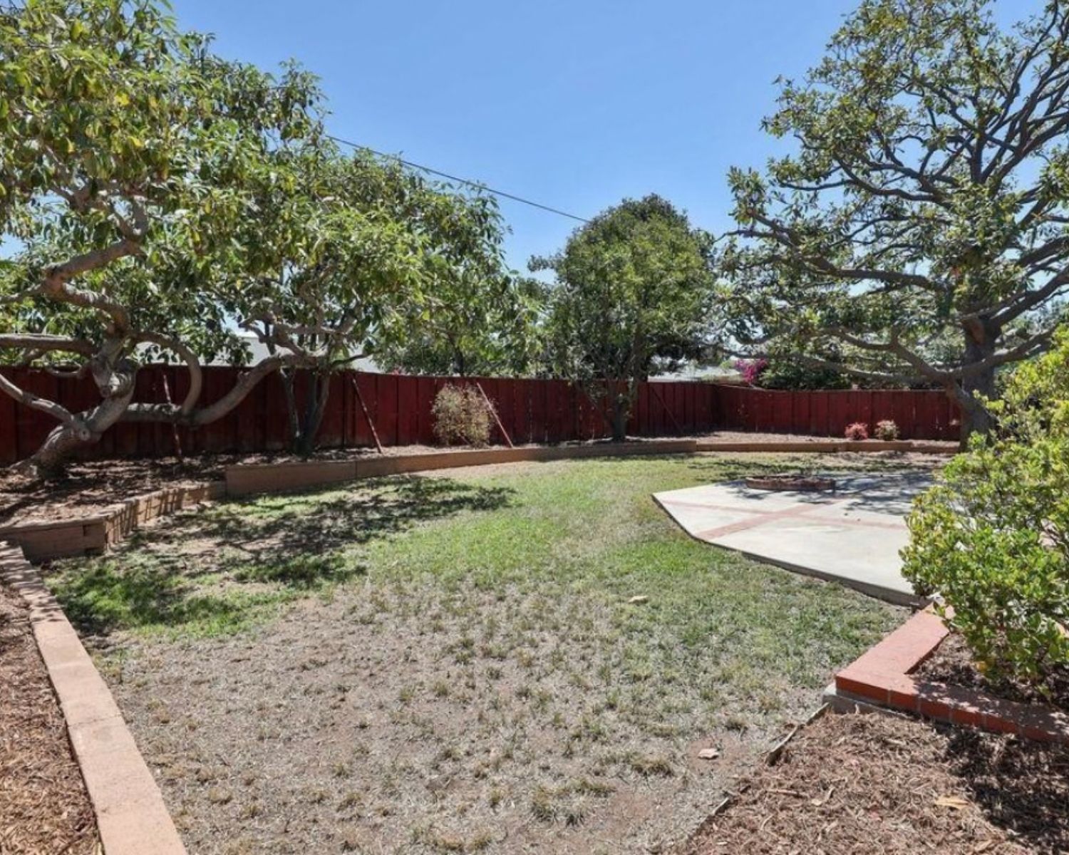 Backyard before renovation with dry patchy grass, a concrete patio and a red wood fence