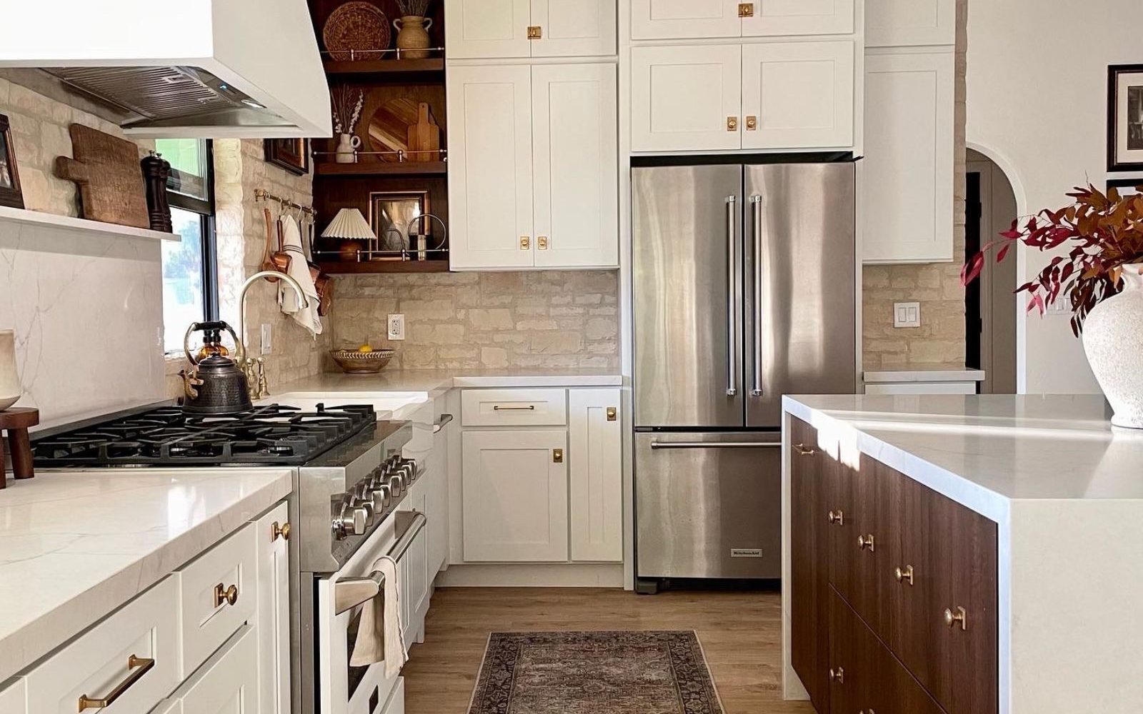 Renovated kitchen with white shaker cabinets, brass hardware, marble countertops, stone backsplash, and walnut island — a finished example of a thoughtfully budgeted home renovation.